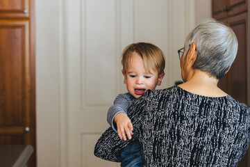 Grandmother Carrying Unhappy Grandson At Home - Powered by Adobe