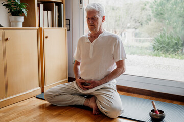 Senior man meditating by Tibetan Singing Bowl at home