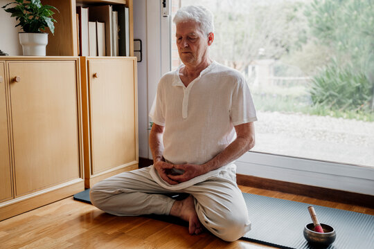 Senior man meditating by Tibetan Singing Bowl at home