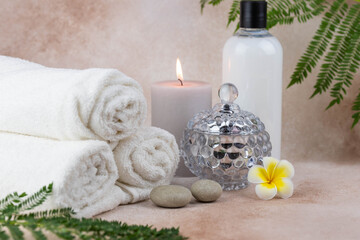Fototapeta na wymiar Spa still life treatment composition on massage table in wellness center. Twisted hot towel with aromatic candles on beige background. Aroma therapy setting. Concept of harmony, balance and meditation