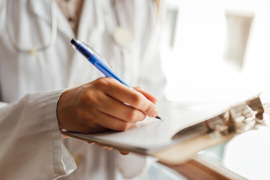 Female doctor writing medical record on clipboard