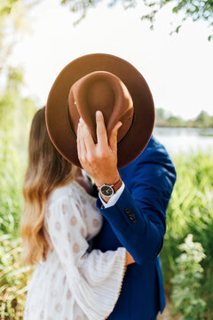 Man embracing girlfriend while hiding behind hat at park