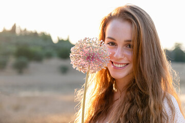 Smiling redhead woman with garlic flower on sunny day