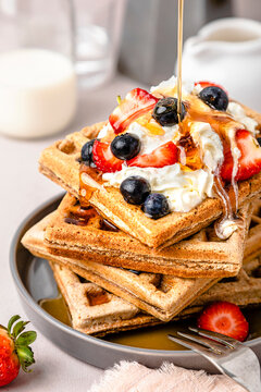 Maple syrup pouring on stack of fresh waffles with blueberries, strawberries and ice cream