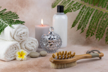 Spa still life treatment composition on massage table in wellness center. Twisted hot towel with aromatic candles and brush on beige background. Aroma therapy setting.