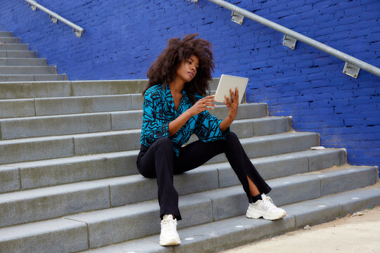 Afro woman using digital tablet while sitting on staircase