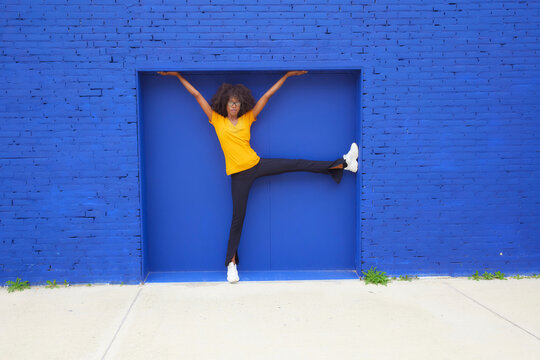 Playful woman with hands raised leaning on blue wall