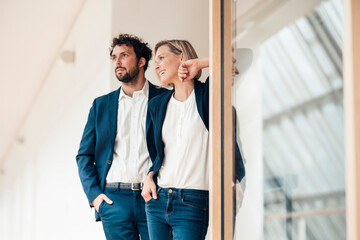 Smiling business partners standing with hand in pocket at office