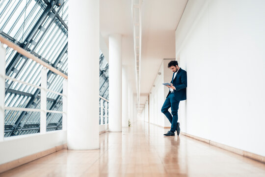 Male entrepreneur using digital tablet while standing at office corridor