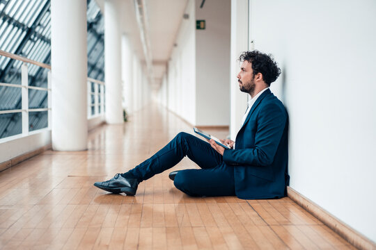 Businessman with digital tablet looking away while sitting at office corridor