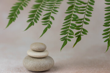 Fototapeta na wymiar Pyramids of gray zen pebble meditation stones with green leaves on beige background. Concept of harmony, balance and meditation, spa, massage, relax.