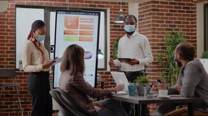 Colleagues presenting business strategy with analysis on monitor during coronavirus pandemic. People with face mask planning development project for company growth at briefing conference. - Powered by Adobe
