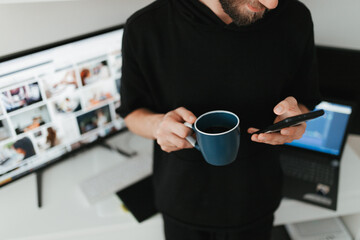 Millennial man having a cup of coffee and surfing net before work on computer and laptop