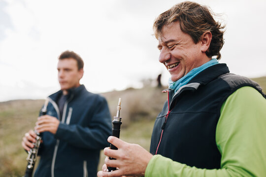 Happy man looking at musical instrument with male friend in background