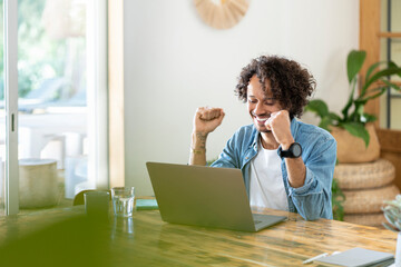 Ecstatic male professional celebrating success in front of laptop at home
