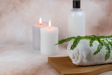 Spa still life treatment composition on massage table in wellness center. Twisted hot towel with aromatic candles on beige background. Aroma therapy setting. Concept of harmony, balance and meditation