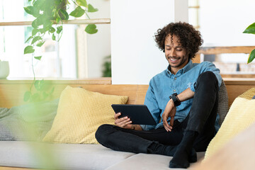Happy male entrepreneur holding digital tablet while sitting on sofa in living room at home
