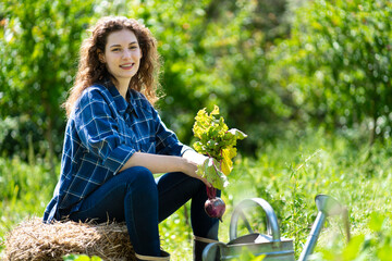 Smiling young woman sitting on stack of hay while holding beetroot plant