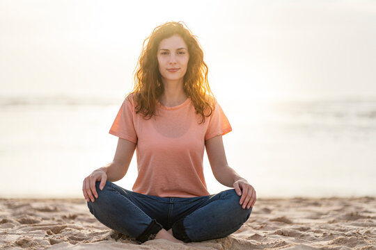 Young Woman With Cross Legs Sitting On Sand At Beach