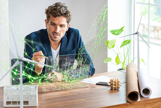 Male architect using futuristic digital tablet while sitting by desk