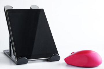 Red computer mouse and black digital tablet on a stand. White background. The concept of using a wireless computer mouse with modern mobile gadgets. Wireless technology and freelance concept
