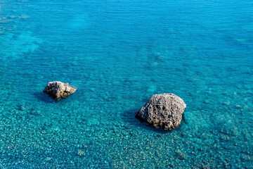 marine background, transparent blue coastal littoral over coral reef and two rocks rise above the water