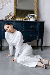 Young woman posing while sitting on the floor in a white dress Bride and a bouquet of flowers on the table