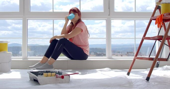 Caucasian woman decorating wall doing house renovation. A female painter taking a break on the floor in front of a painted wall in an apartment. Home improvement concept. New home concept. 4k slow mot