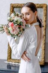 Young bride with a bouquet of flowers in her hands White dress on her body Morning preparations before the engagement ceremony
