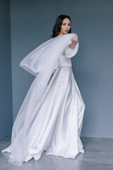 Fototapeta na wymiar Young beauiful happy bride wearing white wedding dress and posing in bright empty interior