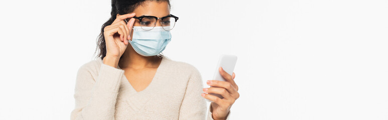 African american woman in eyeglasses and medical mask using cellphone isolated on white, banner.
