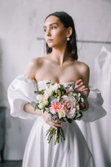 Naklejka premium Beautiful bride in a white dress holding wedding flowers in her hands posing at the camera Portrait of a brunette woman