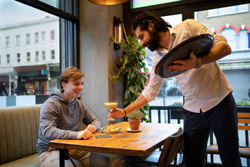Male waiter serving drink to young customer in bar
