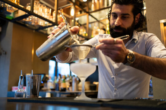 Young male bartender pouring drink in glass at bar counter