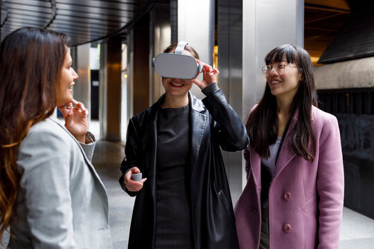 Smiling colleagues looking at businesswoman using virtual reality headset on walkway - Powered by Adobe