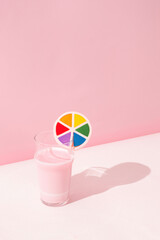 Glass with pink milkshake with lgbt rainbow flag sign on it on white and pink background. Close up perspective, embrace diversity and sexual freedoms concept.