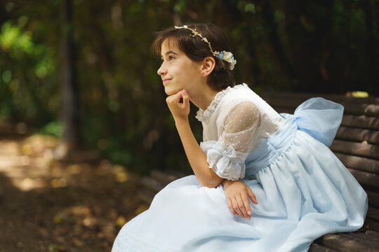 Girl in white communion dress day dreaming while sitting on park bench