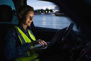 Female professional using laptop while sitting in car at dusk