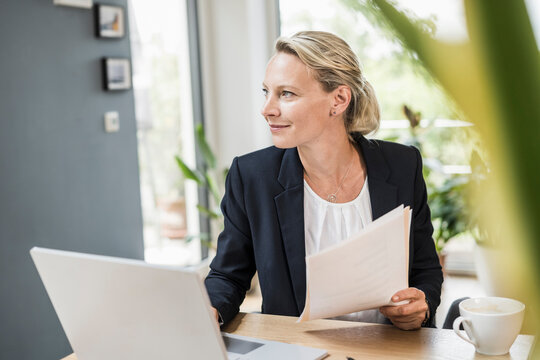 Thoughtful businesswoman with document and laptop at office