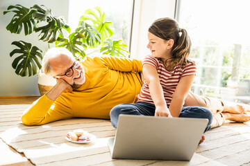 Smiling granddaughter showing laptop to grandfather while sitting at home