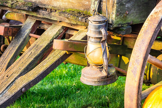 An old antique lantern handing on the side of a wagon in morning sunlight.