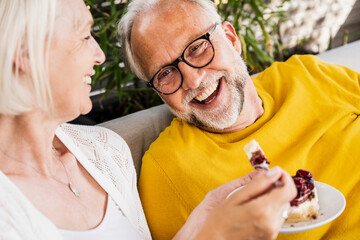 Cheerful man sitting by woman eating dessert on sofa