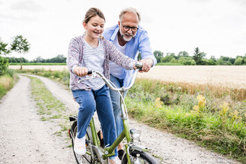 Grandfather teaching cycling to granddaughter on dirt road