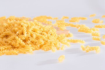 Uncooked Fusilli Pasta Scattered on Wooden Board and White Table. Raw and Dry Macaroni. Fat and...