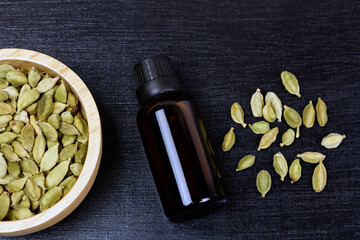 Cardamom essential oil in glass bottle with dry cardamom spice on wooden bowl on black wooden...