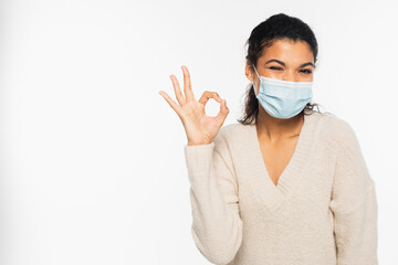 African american woman in medical mask winking and showing ok sign isolated on white.