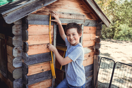 Smiling boy measuring wooden rabbit hutch with tool in back yard