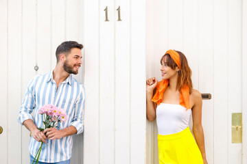 Young man with bunch of flowers looking at woman standing in front of door