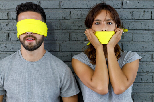 Girlfriend covering mouth with cloth while standing by blindfolded boyfriend in front of wall