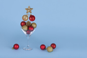 Cocktail glass with flying Christmas bauble balls on blue background. Minimal Christmas party idea.